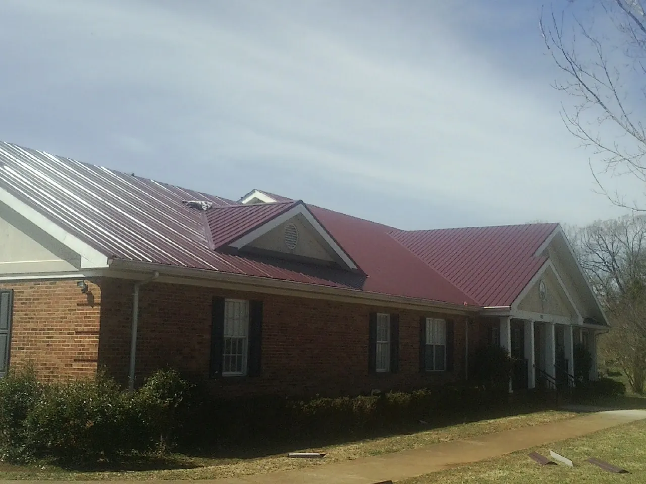 Red metal roof with gabled entries on a long brick building, from a Hail Damage Roof Repair job in Peoa