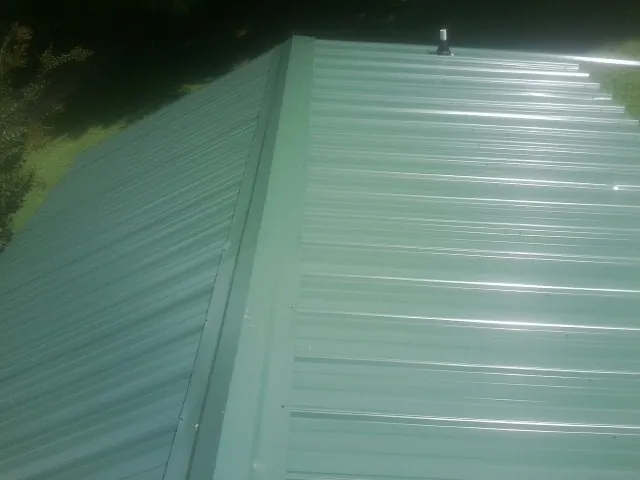 New green metal panels meeting at the ridge of a roof — Flat Roof Repair work by our crew in Peoa