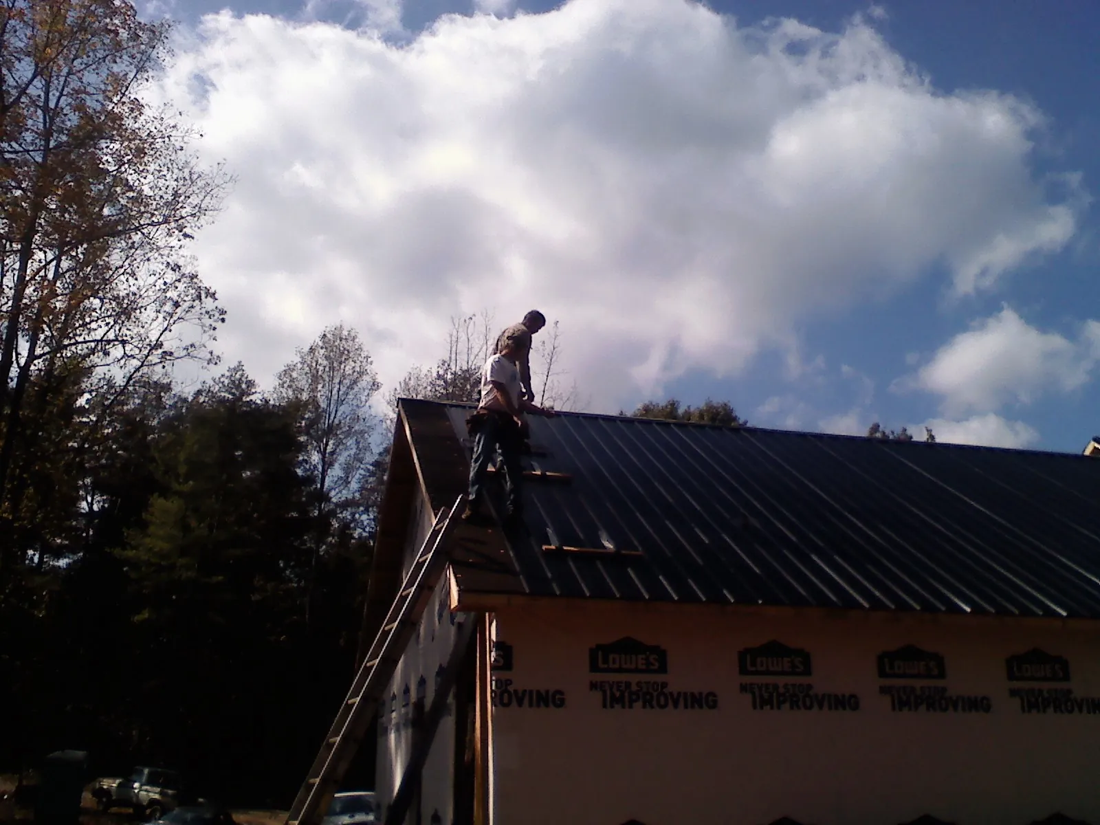 Roofer fastening dark metal panels high against a cloudy sky, from a Roof Inspection job in Peoa