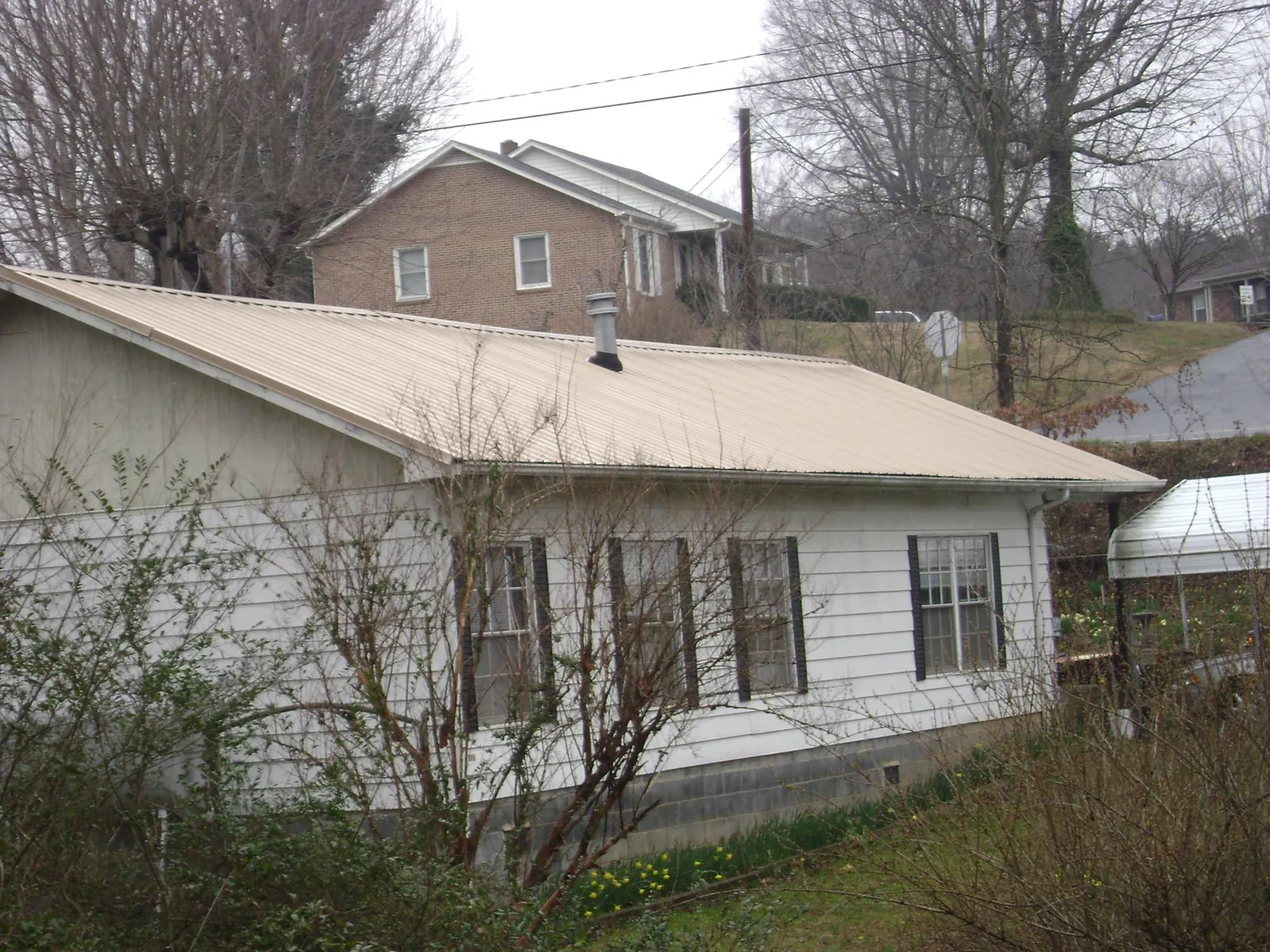 Tan metal roof on a white sided house set into a hillside — Commercial Roofing by Roofing Brothers in Peoa