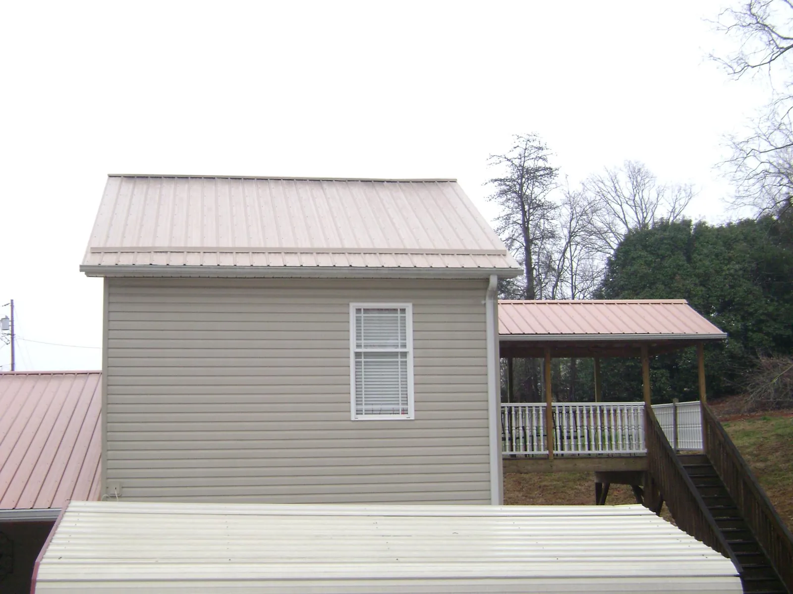 Tan metal roofs on a two story addition and attached porch, from a Roof Replacement job in Peoa